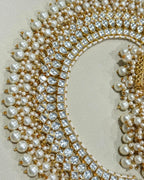 A close-up of an ornate gold and pearl Pachi kundan necklace, arranged on a neutral beige background.