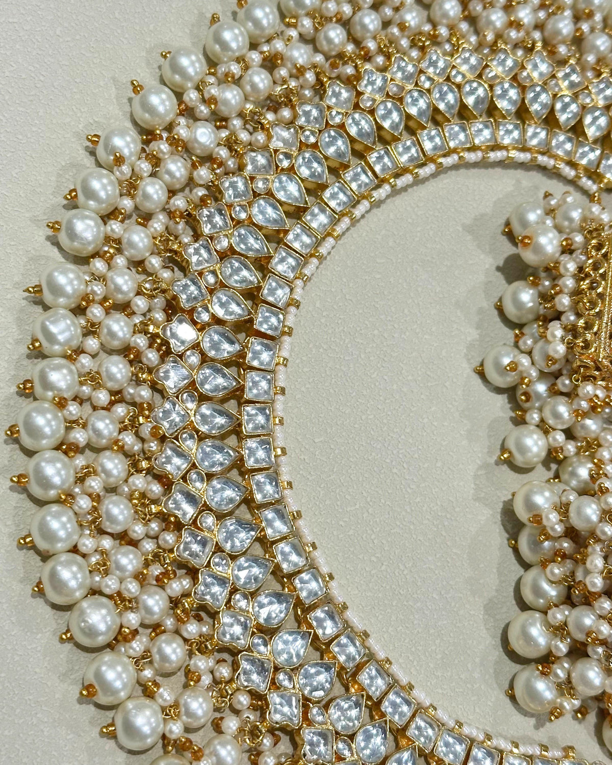 A close-up of an ornate gold and pearl Pachi kundan necklace, arranged on a neutral beige background.