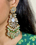 A close-up of a model wearing a Medium gold-toned dangle earring decorated with white MOP, aqua beads, and dangling Aqua seed drops, paired with a green patterned top.